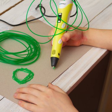 A child draws a three-dimensional figure with a 3D pen made of green plastic.