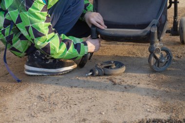 Bir adam eski kırık bir bebek arabasının tekerleğini yenisiyle değiştiriyor..