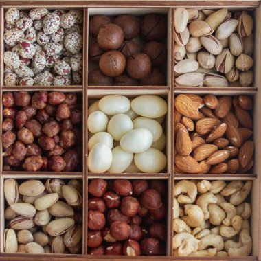 Ahşap bir kutuda bir sürü fındık çeşidi vardır: fındık, fıstık, şam fıstığı, badem, macadamia, kaju..