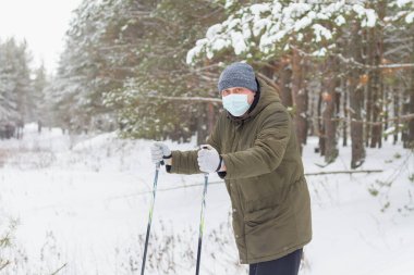 Kendini virüsten korumak için tıbbi maske takan tuhaf bir adam kışın kayaklarla ormanda dolaşıyor..