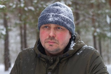 Kışın ormanda, sıcak kıyafetler ve karda bir şapkayla gezen Avrupalı bir adamın portresi..