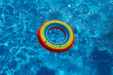 Havuzda parlak mavi suyla birlikte renkli gökkuşağı şişme daire. Boşluğu kopyala.