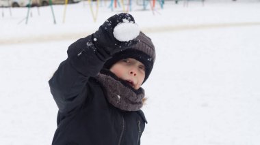 Kışın giysili bir çocuk, kışın yürüyüş yapan bir arkadaşına bir tutam karla saldırır..