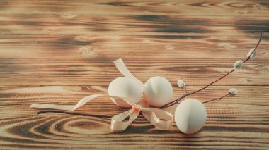 Paskalya beyaz yumurtaları, kahverengi ahşap bir masada Paskalya bayramı için söğüdü olan bir kurdeleyle bağlanır..