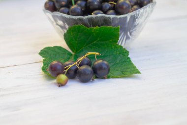 Frenk üzümlü, beyaz ahşap bir masada cam bir kasede olgun siyah üzümlü üzümler..