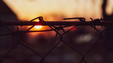 Gün batımında dikenli telle örülmüş bir ızgara hapis ve özgürlüğün sembolü olarak.