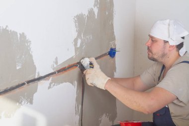 Beyaz bir erkek müteahhit bir elektrik kutusunu alçı ya da kaymaktaşı olan bir prizin altında emniyete alıyor..