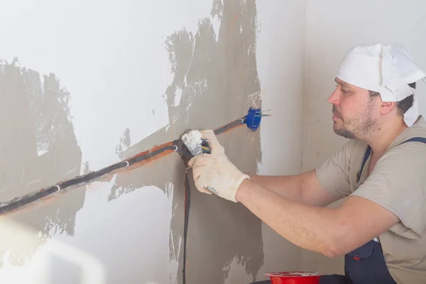 A Caucasian male builder secures an electrical box under an outlet with plaster or alabaster.