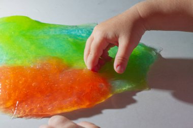 Çocuk kırmızı ve yeşil bir balçıkla oynar, bebek balçığı eliyle ezer..