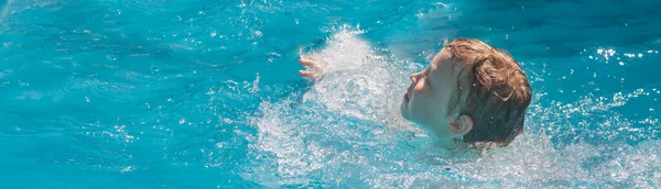 A Caucasian boy of 7 years old learns to swim in the pool in the summer, water splashes fly to the sides.