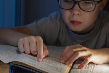 Gözlüklü genç bir beyaz çocuk kitap okumakta zorlanıyor ve metni anlamlandırmaya çalışıyor..