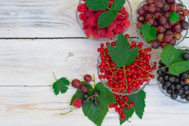 Beyaz ahşap arka planda farklı meyve tabakları. Olgun, sulu, kırmızı frenk üzümü, kara frenk üzümü, bektaşi üzümü, yeşil yapraklı ahududu..