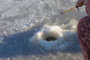 Nehir veya gölün buzunda kış balıkçılığı. Bir balıkçı buzdaki bir delikte balık yakalar..