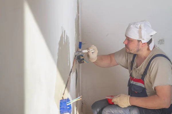 A Caucasian male builder secures an electrical box under an outlet with plaster or alabaster.