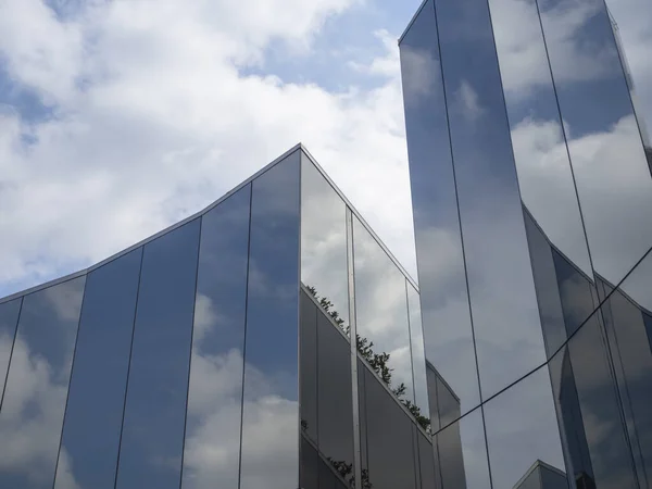 Blue sky with clouds and its reflection in modern glass architecture. Geometric towers covered with a reflective surface. White fluffy clouds.