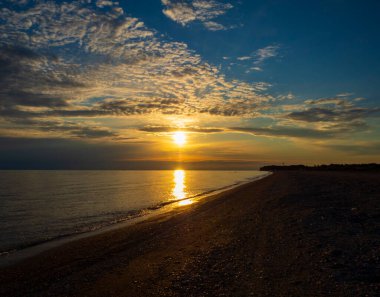 Denizde güzel bir gün batımı, sahilin manzarası. Yanardöner bulutlu mavi gökyüzü. Kumsal ve sakin deniz.