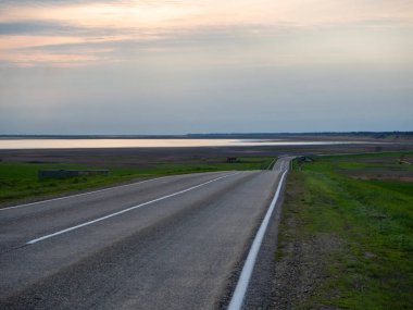 Körfezin yanındaki bozkırdan geçen boş bir yol. Çimlerle, suyla ve gökyüzüyle güzel bir manzara..
