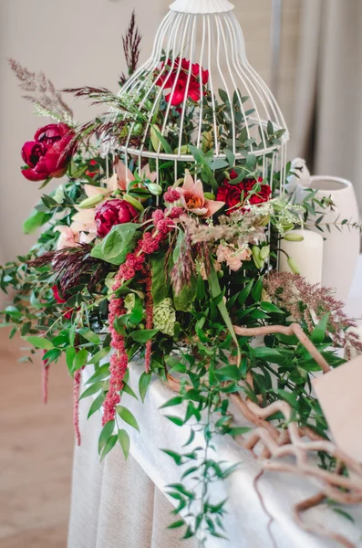 Decoración de ceremonia de boda en restauracióntía. La composición de peonías rojas y rosadas, flores de rosa, eucalipto verde se encuentra en la mesa con mantel blanco. Jaula de pájaro decorada, velas, ramas. Marte —  Fotos de Stock