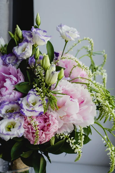 Rich bunch of pink peonies peony and lilac eustoma roses flowers in glass vase on white background. Rustic style, still life.