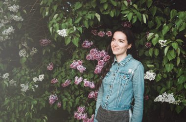 Bir güzel gülümsüyor, genç kadın açık bahar bahçe çiçeği mor Eflatun çiçekli portresi. Şişe su tutarak rahat kot elbise, çekici kadın. kavramı, doğa ve bakım.