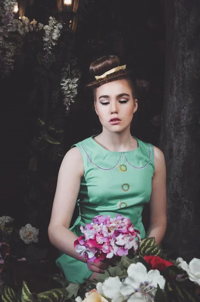 Retrato de jovem bela mulher segurando flor de hortênsia rosa. Menina modelo de moda em vestido ciano verde, penteado elegante, maquiagem, cabelo, estilo de moda. Feminino em floração jardim escuro. Beleza — Fotografia de Stock
