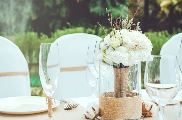 Conjunto de mesa para una fiesta o banquete de recepción de boda. Ramo nupcial de invierno de claveles blancos, peonía, rosas flores con cordel en jarrón sobre fondo artesanal. Elegante copa de vino, cubiertos, servilleta —  Fotos de Stock