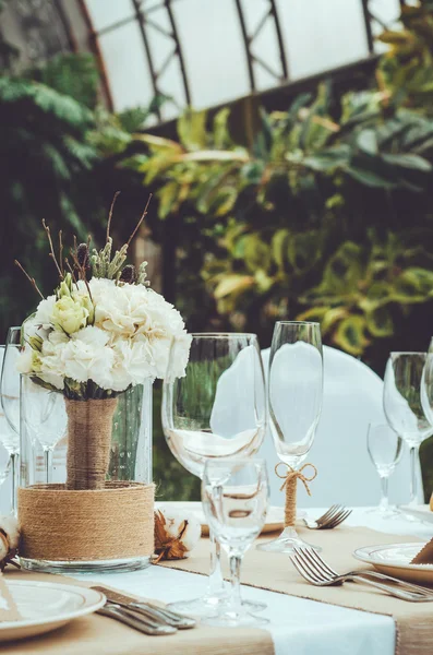 Conjunto de mesa para una fiesta o banquete de recepción de boda. Ramo nupcial de invierno de claveles blancos, peonía, rosas flores con cordel en jarrón sobre fondo artesanal. Elegante copa de vino, cubiertos, servilleta —  Fotos de Stock