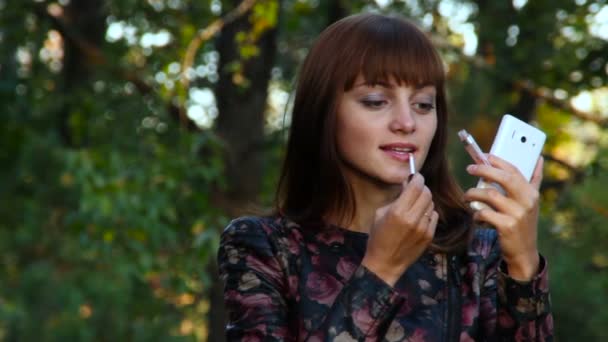 Güzel kadın smartphone vasıl arıyorsunuz dudak parlatıcısı uygulayarak — Stok video