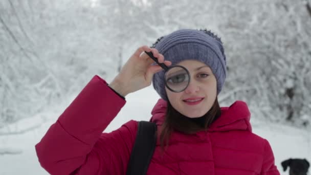 Woman looking through a magnifying glass, snow background — Stock Video