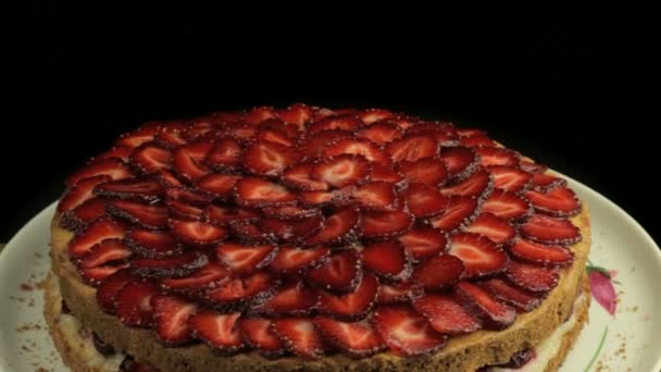 Cut a lot of red strawberry on the cake, slowly rotates counterclockwise on a black background — Stock Video