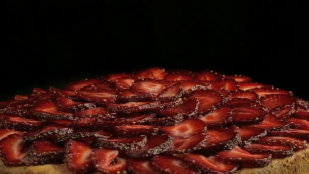 Muitos morangos vermelhos nas peças do bolo, gira lentamente no sentido anti-horário em um fundo preto — Vídeo de Stock