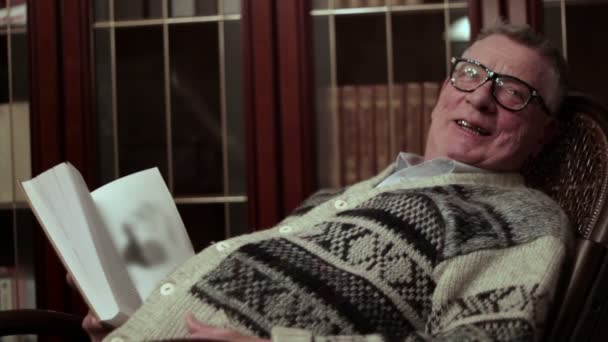 Old man with a book sitting in a rocking chair — Stock Video