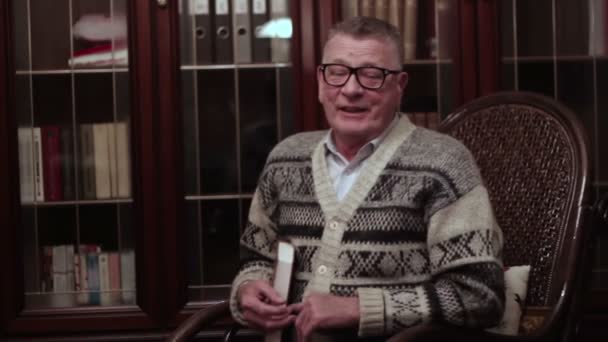 Viejo abuelo balanceándose en una mecedora con un libro — Vídeo de stock