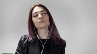 Beyaz arka planda dans eden, kulaklık takan neşeli genç bir kadının portresi.