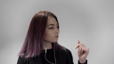 Beyaz arka planda dans eden ve şarkı söyleyen kulaklıklı genç kadının portresi.