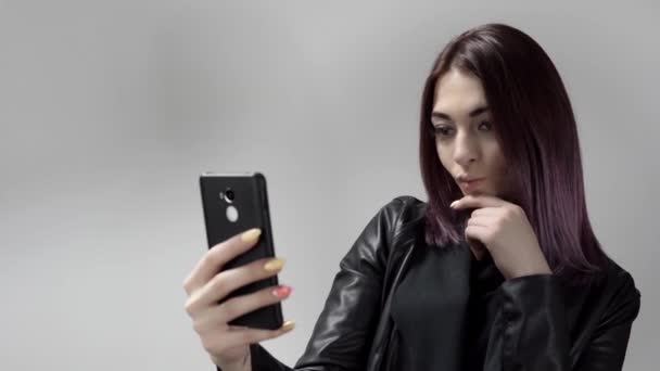 Retrato de una jovencita guapa que hace selfie posando delante de una cámara móvil sobre fondo blanco — Vídeo de stock