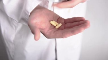 Bir sürü hapı olan bir el ve yakın plan çekimde su toplayan bir doktor.