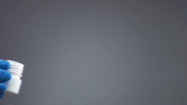 Eldivenli bir el, içinde haplar olan plastik bir kap fırlatır ve yavaş çekimde cam yüzeye dökülür.