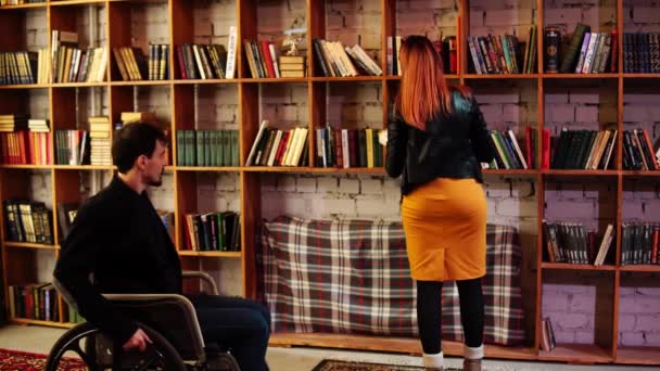 A man in a wheelchair in the library asks a woman to hand him a book — Stock Video