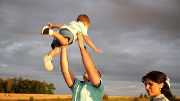 Um homem de pé em um campo com sua esposa está jogando seu filho no ar em lentidão — Vídeo de Stock