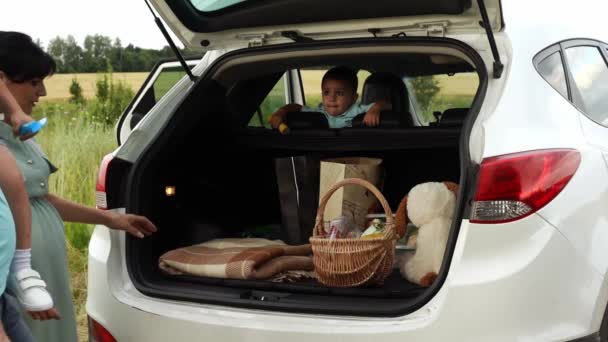 Pár s dětmi dorazily na piknik v poli autem a vyložit zavazadla z kufru v pomalé — Stock video