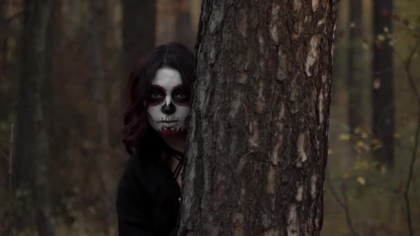 Bruja con maquillaje de santa muerte sale del árbol y se esconde — Vídeo de stock