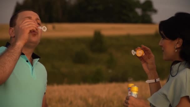 Portretul cuplului fericit la o întâlnire în câmpul de vară suflând bule de săpun în mișcare lentă — Videoclip de stoc