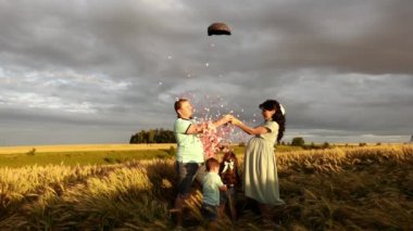 Çocuklu bir çift buğday tarlasında duruyor ve balon patlatıyor gelecekteki bebeğin cinsiyetini öğrenmek için.