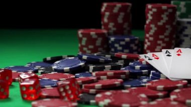 Kırmızı zarlar ve tüm aslar yakın planda yeşil masada poker fişleri yığını üzerinde yatıyor.