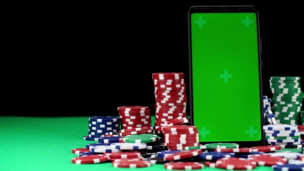 Mobile with green screen in a vertical orientation stands among stacks of poker chips in close-up — Stock Video