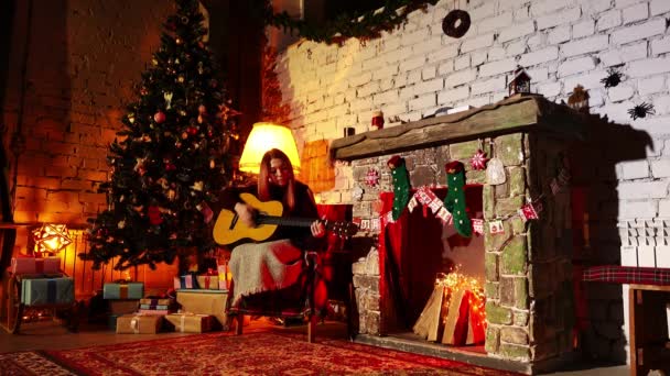 En dam sitter i fåtölj bland nyårsdekorationer och spelar gitarr — Stockvideo