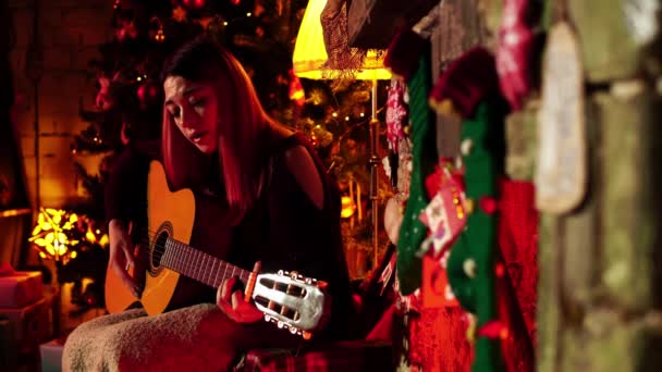 Senhora cantora com uma guitarra sentada em casa na véspera de Natal em close-up — Vídeo de Stock