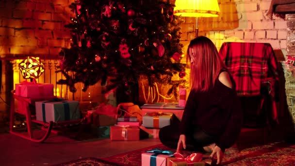 Joyeux jeune femme met des cadeaux de Noël sous l'arbre de Noël au salon sombre confortable — Video