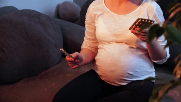 Terhes nő kezében buborékcsomagolás gyógyszerekkel ül egy kanapén a nappaliban, és sóhajt közelről — Stock videók